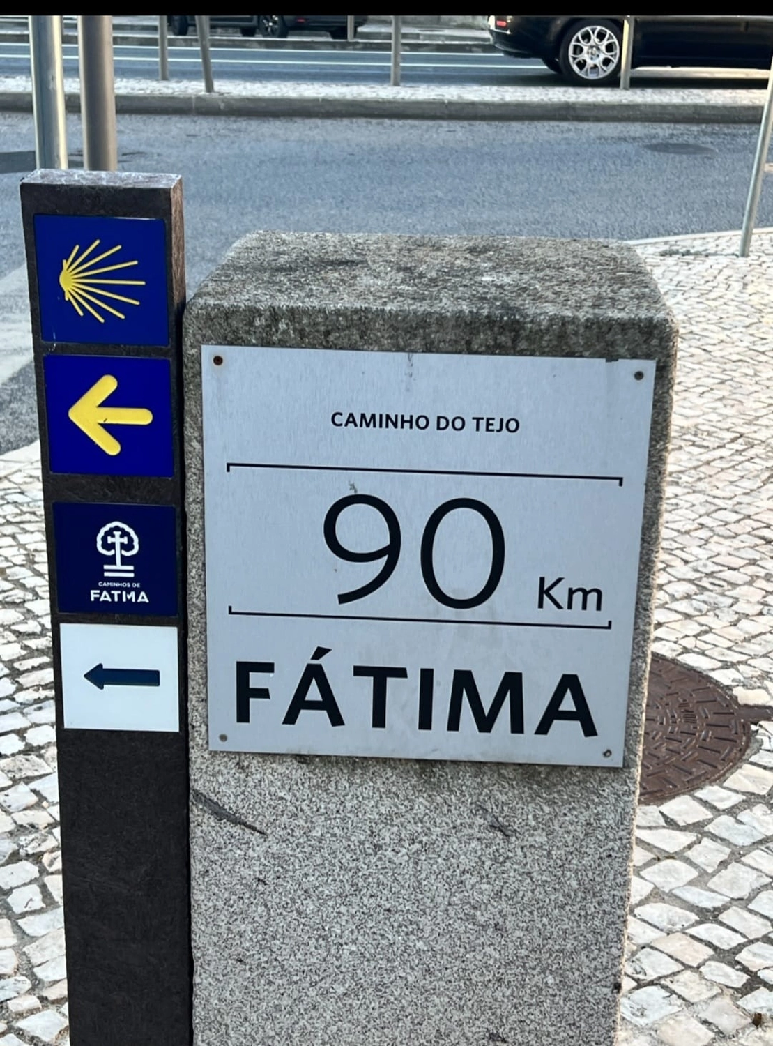 Mit Lida Pilgern - Pilgerreise-Coaching - Eine steinerne Wegmarkierung in Portugal, die 90 Kilometer nach Fátima entlang des „Caminho do Tejo“ anzeigt, mit einer gelben Jakobsmuschel und Richtungspfeilen.